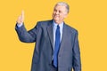 Senior grey-haired man wearing business jacket looking proud, smiling doing thumbs up gesture to the side Royalty Free Stock Photo