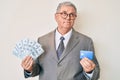 Senior grey-haired man wearing business suit holding credit car and dollars smiling looking to the side and staring away thinking Royalty Free Stock Photo