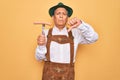 Senior grey-haired man wearing german traditional octoberfest suit holding fork with sausage with angry face, negative sign