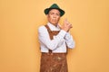 Senior grey-haired man wearing german traditional octoberfest suit over yellow background Holding symbolic gun with hand gesture, Royalty Free Stock Photo