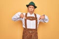 Senior grey-haired man wearing german traditional octoberfest suit over yellow background Pointing down looking sad and upset, Royalty Free Stock Photo