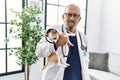 Senior grey-haired man wearing veterinarian uniform holding chihuahua with elizabethan collar at vet clinic Royalty Free Stock Photo