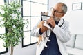 Senior grey-haired man wearing veterinarian uniform holding chihuahua with elizabethan collar at vet clinic Royalty Free Stock Photo