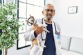 Senior grey-haired man wearing veterinarian uniform holding chihuahua with elizabethan collar at vet clinic Royalty Free Stock Photo