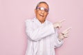 Senior grey-haired scientist man wearing glasses and coat over isolated pink background smiling and looking at the camera pointing Royalty Free Stock Photo