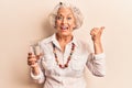 Senior grey-haired woman drinking glass of water pointing thumb up to the side smiling happy with open mouth Royalty Free Stock Photo