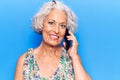 Senior grey-haired woman having conversation talking on the smartphone looking positive and happy standing and smiling with a Royalty Free Stock Photo