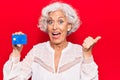 Senior grey-haired woman holding credit card pointing thumb up to the side smiling happy with open mouth Royalty Free Stock Photo