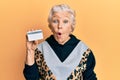 Senior grey-haired woman holding credit card scared and amazed with open mouth for surprise, disbelief face Royalty Free Stock Photo