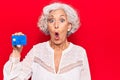 Senior grey-haired woman holding credit card scared and amazed with open mouth for surprise, disbelief face Royalty Free Stock Photo