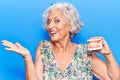 Senior grey-haired woman holding denture celebrating achievement with happy smile and winner expression with raised hand Royalty Free Stock Photo