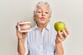 Senior grey-haired woman holding green apple and denture teeth looking at the camera blowing a kiss being lovely and sexy Royalty Free Stock Photo