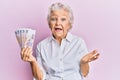 Senior grey-haired woman holding russian 100 ruble banknotes celebrating achievement with happy smile and winner expression with Royalty Free Stock Photo