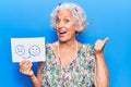 Senior grey-haired woman holding sad to happy emotion paper pointing thumb up to the side smiling happy with open mouth Royalty Free Stock Photo