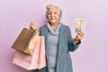 Senior grey-haired woman holding shopping bags and uk pounds banknotes relaxed with serious expression on face