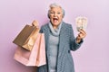 Senior grey-haired woman holding shopping bags and uk pounds banknotes smiling and laughing hard out loud because funny crazy joke