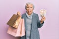 Senior grey-haired woman holding shopping bags and uk pounds banknotes sticking tongue out happy with funny expression