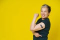 Senior grey haired woman rebelling showing nude shoulder with dark band aid or plaster on it isolated on yellow