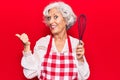 Senior grey-haired woman wearing apron holding whisk pointing thumb up to the side smiling happy with open mouth Royalty Free Stock Photo