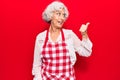 Senior grey-haired woman wearing apron pointing thumb up to the side smiling happy with open mouth Royalty Free Stock Photo