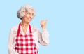 Senior grey-haired woman wearing apron smiling with happy face looking and pointing to the side with thumb up Royalty Free Stock Photo