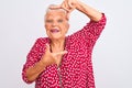 Senior grey-haired woman wearing red casual jacket standing over isolated white background smiling making frame with hands and Royalty Free Stock Photo