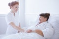 Senior grey woman lying in white hospital bed with young helpful nurse holding her hand Royalty Free Stock Photo