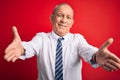 Senior handsome businessman wearing elegant tie standing over isolated red background looking at the camera smiling with open arms Royalty Free Stock Photo