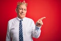 Senior handsome businessman wearing king crown standing over isolated red background with a big smile on face, pointing with hand Royalty Free Stock Photo