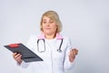 Senior handsome doctor, woman with blonde hair, wearing medical uniform, looking on sheet folder with prescription. Confused Royalty Free Stock Photo