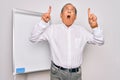 Senior handsome grey-haired businessman doing presentation using magnetic board amazed and surprised looking up and pointing with Royalty Free Stock Photo