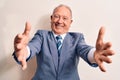 Senior handsome grey-haired businessman wearing elegant suit over white background looking at the camera smiling with open arms Royalty Free Stock Photo