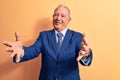 Senior handsome grey-haired businessman wearing elegant suit over yellow background looking at the camera smiling with open arms Royalty Free Stock Photo