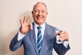 Senior handsome grey-haired businessman wearing suit drinking glass of water to refreshment doing ok sign with fingers, smiling Royalty Free Stock Photo