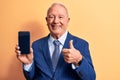 Senior handsome grey-haired businessman wearing suit holding smartphone showing screen smiling happy and positive, thumb up doing Royalty Free Stock Photo