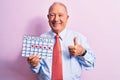 Senior handsome grey-haired businessman wearing tie holding cardio heart calendar smiling happy and positive, thumb up doing Royalty Free Stock Photo