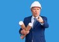 Senior handsome grey-haired man wearing architect hardhat holding blueprints pointing with finger to the camera and to you, Royalty Free Stock Photo