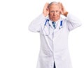 Senior handsome grey-haired man wearing doctor coat and stethoscope doing bunny ears gesture with hands palms looking cynical and Royalty Free Stock Photo