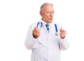 Senior handsome grey-haired man wearing doctor coat and stethoscope doing money gesture with hands, asking for salary payment, Royalty Free Stock Photo