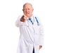 Senior handsome grey-haired man wearing doctor coat and stethoscope pointing displeased and frustrated to the camera, angry and