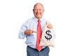 Senior handsome grey-haired man wearing elegant clothes holding money bag smiling happy pointing with hand and finger Royalty Free Stock Photo