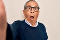 Senior handsome grey-haired man wearing sweater and glasses making selfie by camera scared in shock with a surprise face, afraid Royalty Free Stock Photo