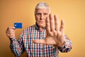Senior handsome hoary customer man holding credit card to finance payment with open hand doing stop sign with serious and