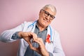 Senior handsome hoary doctor man wearing stethoscope and red HIV ribbon on coat smiling in love showing heart symbol and shape Royalty Free Stock Photo