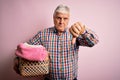 Senior handsome hoary man doing housework holding wicker basket with clothes with angry face, negative sign showing dislike with