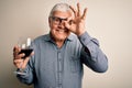 Senior handsome hoary man drinking glass of red wine over isolated white background with happy face smiling doing ok sign with