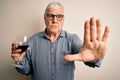 Senior handsome hoary man drinking glass of red wine over isolated white background with open hand doing stop sign with serious Royalty Free Stock Photo