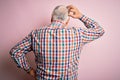 Senior handsome hoary man wearing casual colorful shirt over isolated pink background Backwards thinking about doubt with hand on