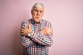 Senior handsome hoary man wearing casual colorful shirt over isolated pink background shaking and freezing for winter cold with Royalty Free Stock Photo