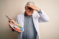 Senior handsome hoary painter man painting using brush and palette with colors stressed with hand on head, shocked with shame and Royalty Free Stock Photo